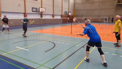 Kilka osób gra w badmintona w sali sportowej.
